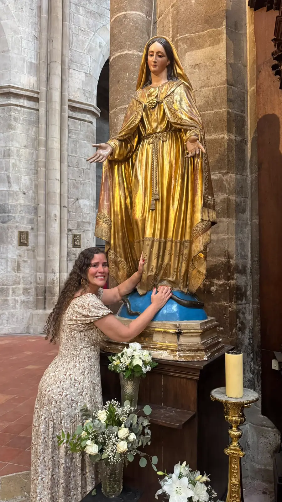 Hérica emocionada tocando os pés da imagem dourada de Maria
