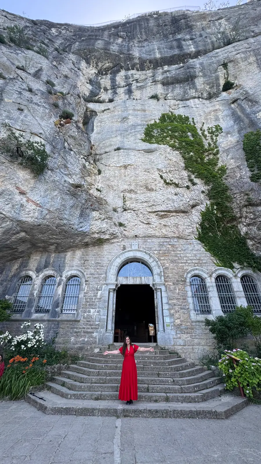 Hérica de braços abertos na escadaria da gruta, sob a rocha
